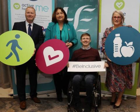 Photo of a man and two women standing and a man in a wheelchair, all holding Active Healthy me signs